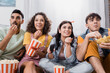 © LIGHTFIELD STUDIOS - cheerful hispanic friends eating popcorn and chips while watching tv
