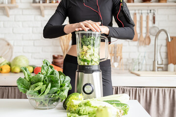 Young blond smiling woman making green smoothie at home kitchen