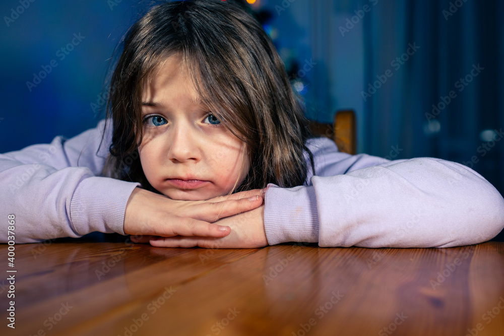 Smutna dziewczynka siedząca przy stole w czasie świąt bożego narodzenia.  - obrazy, fototapety, plakaty 