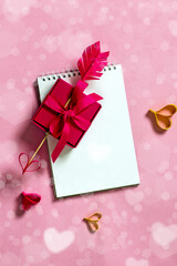 Wall Mural - Valentine's day background from notepad, arrow heart and gift box. Valentine's day romantic background concept from gift box with homemade arrow with paper heart. Top view, copy space