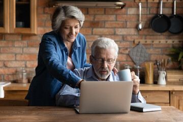 smiling older mature hoary woman pointing finer at laptop screen, choosing holidays trip with relaxe