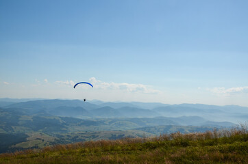 Paraglider flying over Carpathian mountains against clear sky in summer day