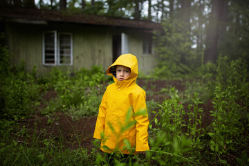 A child in a yellow coat standing in the woods in front of an old wooden house