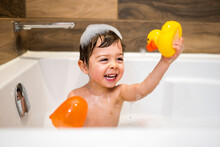 Happy Two Year Kid Bathes With Toys In Bath With Foam And Duck,