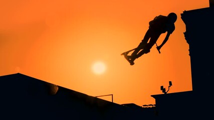 Wall Mural - Slow motion: unrecognizable teenage boy silhouette showing high jump tricks on scooter against orange sunset sky at skatepark. Sport, extreme, freestyle, outdoor activity concept