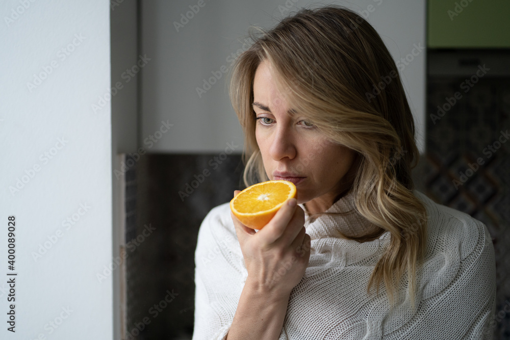 Sick woman trying to sense smell of  half fresh orange, has symptoms of Covid-19, corona virus infection - loss of smell and taste. One of the main signs of the disease.  - obrazy, fototapety, plakaty 