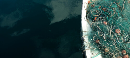 Fishing net in a small fishing boat. Horizontal panoramic crop with large area of dark blue water.