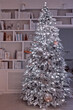 flocked illuminated christmas tree in front of the bookcase, cozy home interior