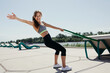 © DmitryStock - Young woman with red hair in grey top and black leggins doing exercises with elastic fitness tape outside.