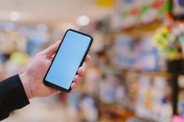 Wall Mural - Mock-up technology. The guy holds a smartphone in his hands on the background supermarket.