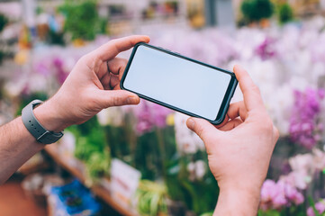 Wall Mural - Mock-up technology. The guy holds a smartphone in his hands on the background flowers.