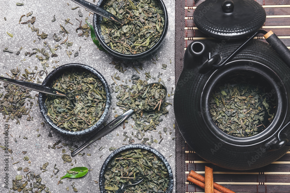 Bowls and teapot with dry green tea on dark background
