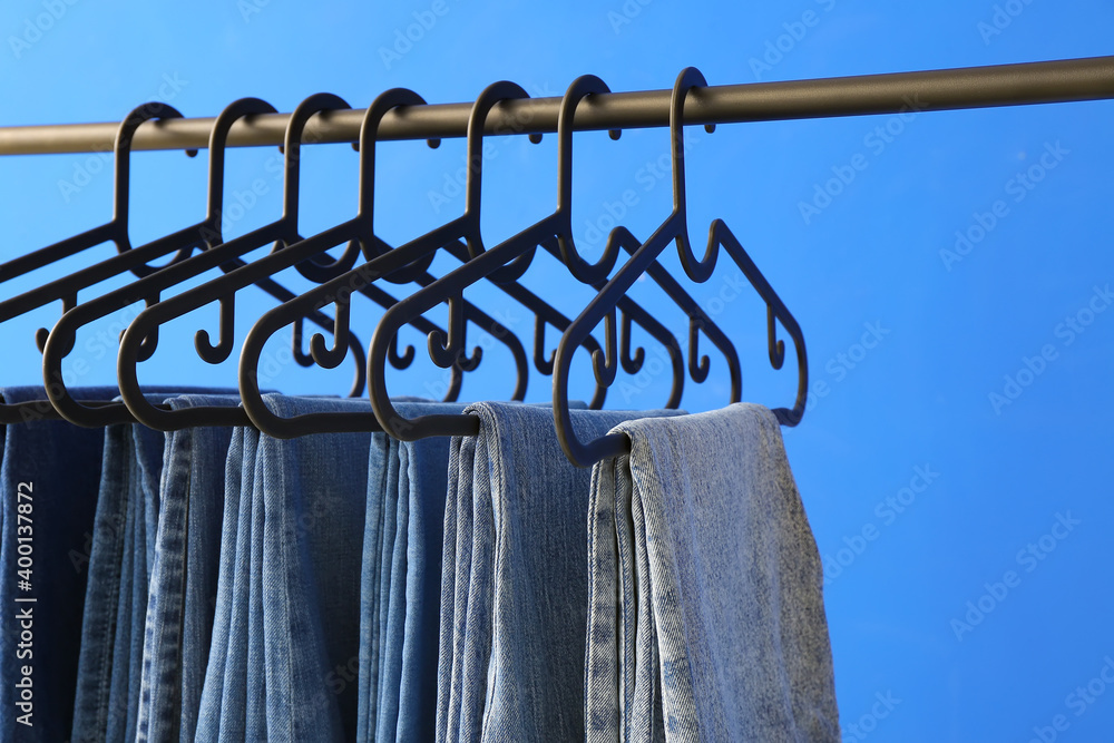 Clothes rack with jeans on color background