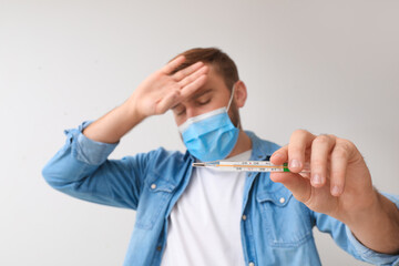 Ill man measuring his temperature on light background. Coronavirus epidemic