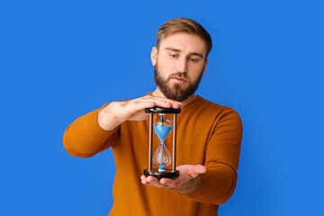 Canvas Print - Young man with hourglass on color background