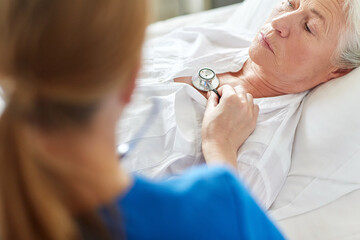 Poster - medicine, healthcare and old age concept - female doctor or nurse with stethoscope checking heartbeat or breath of senior woman at hospital