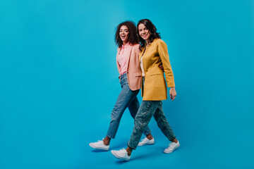 Poster - Two brunette girl walking across studio. Indoor full length portrait of female models in jeans.