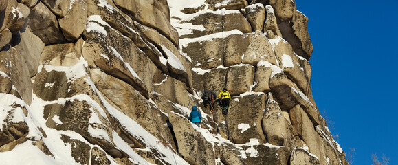 Wall Mural - A huge rock illuminated by sunlight with figures of three mountaineers in the center during a winter ascent in the mountains, panorama.