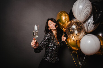 Wall Mural - Positive smiling girl dancing on black background. Emotional latin young woman enjoying champagne.