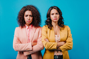 Wall Mural - Disappointed girls looking to camera. Indoor photo of two brunette women standing on studio background.