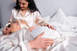 Pregnant woman touching belly near Hispanic partner on bed on blurred background