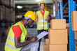 © bung - A Man worker writing address from the parcel on paper on the clipboard in automotive parts warehouse center. Engineers people wear a safety helmet. There are many goods on the floor