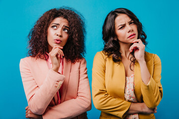 Wall Mural - Front view of pensive girls. African woman and latin lady posing on blue background.