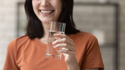 I recommend. Close up of young woman holding glass of pure fresh natural water in hand advertising demonstrating it to spectator. Cropped portrait of smiling lady promoting healthy lifestyle nutrition