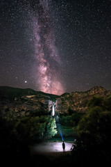 Wall Mural - Man silhouette illuminating a waterfall and observing the milky way. Nice night image Illuminating a waterfall and observing the stars and the Milky Way. Night landscape.
