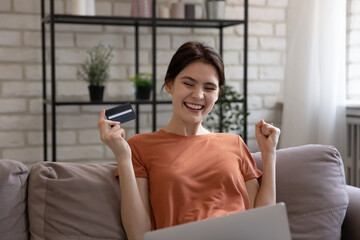 Money was sent. Happy young woman sitting on sofa holding plastic card providing loan mortgage bill payment online. Smiling e-bank user customer satisfied with easy quick successful transfer using app