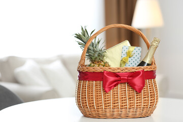 Wicker basket full of gifts on white table in living room. Space for text