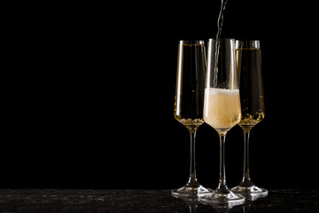 three glasses filled with sparkling wine on a black background.