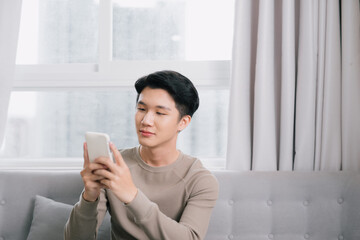 Wall Mural - Happy Young Man Relaxing On Sofa And Looking At Cellphone