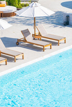 Umbrella And Deck Chair Around Outdoor Swimming Pool In Hotel Resort