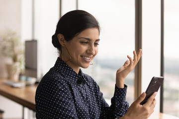 Wall Mural - Close up of happy millennial Indian woman look at smartphone screen talk on video call online. Smiling young ethnic female use cellphone, text or message on web on gadget. Technology concept.