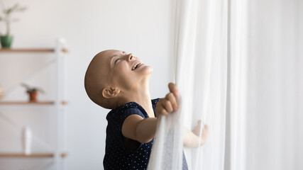 Wall Mural - Amazing wonder of life. Happy young hairless female open curtain on window enjoy light sun beautiful day will to live. Millennial woman cancer patient laugh excited with good news remission recovery