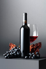 Wall Mural - Red wine and blue grapes with dried up vine leaves on a dark background.