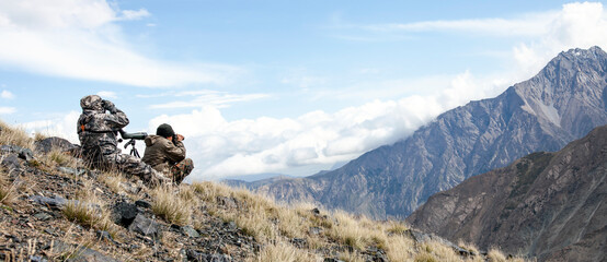 two men in camouflage conduct surveillance high in the mountains.