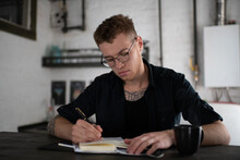 Captivated Man In Eyeglasses Writing In Notebook At Table