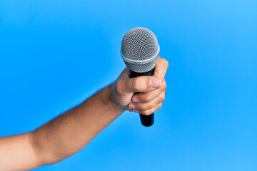 Canvas Print - Hand of hispanic man holding microphone over isolated blue background.