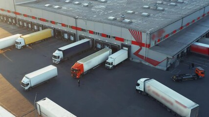 Wall Mural - Trucks with semi-trailers stand at warehouse ramps in the logistics park with loading hub and wait for load and unload goods at sunset. Aerial view