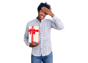 Poster - Handsome african american man with afro hair holding gift stressed and frustrated with hand on head, surprised and angry face