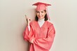© Krakenimages.com - Young caucasian woman wearing graduation cap and ceremony robe with a big smile on face, pointing with hand and finger to the side looking at the camera.