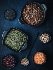 Black bowls of various dried legumes on dark blue background. Overhead shot.