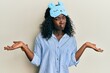 © Krakenimages.com - Beautiful african young woman wearing sleep mask and pajama clueless and confused expression with arms and hands raised. doubt concept.