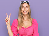 Fototapeta Do pokoju - Beautiful caucasian woman wearing sunglasses and summer style smiling with happy face winking at the camera doing victory sign. number two.