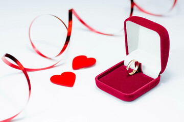 Gold ring, wedding ring in red box and, red heart on white-red background with beautiful bokeh. The moment of a wedding, anniversary, engagement, or Valentine's Day. Happy day.