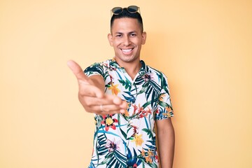 Wall Mural - Young handsome latin man wearing summer clothes smiling friendly offering handshake as greeting and welcoming. successful business.