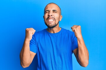 Poster - Hispanic adult man wearing casual blue t shirt celebrating surprised and amazed for success with arms raised and eyes closed