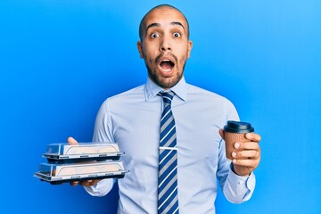 Poster - Hispanic adult business man holding take away coffee and sweets afraid and shocked with surprise and amazed expression, fear and excited face.